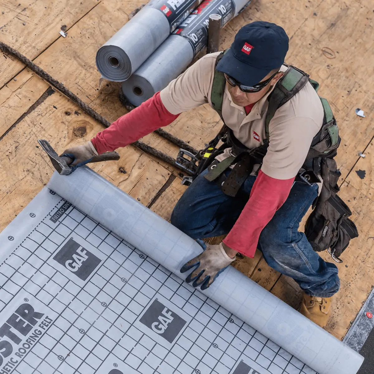 Roofer unrolling synthetic underlayment over plywood