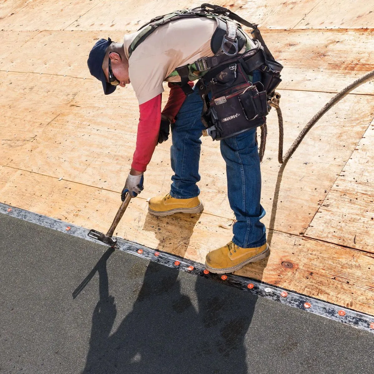 Roofer rolling out leak barrier along the edge of a roof deck