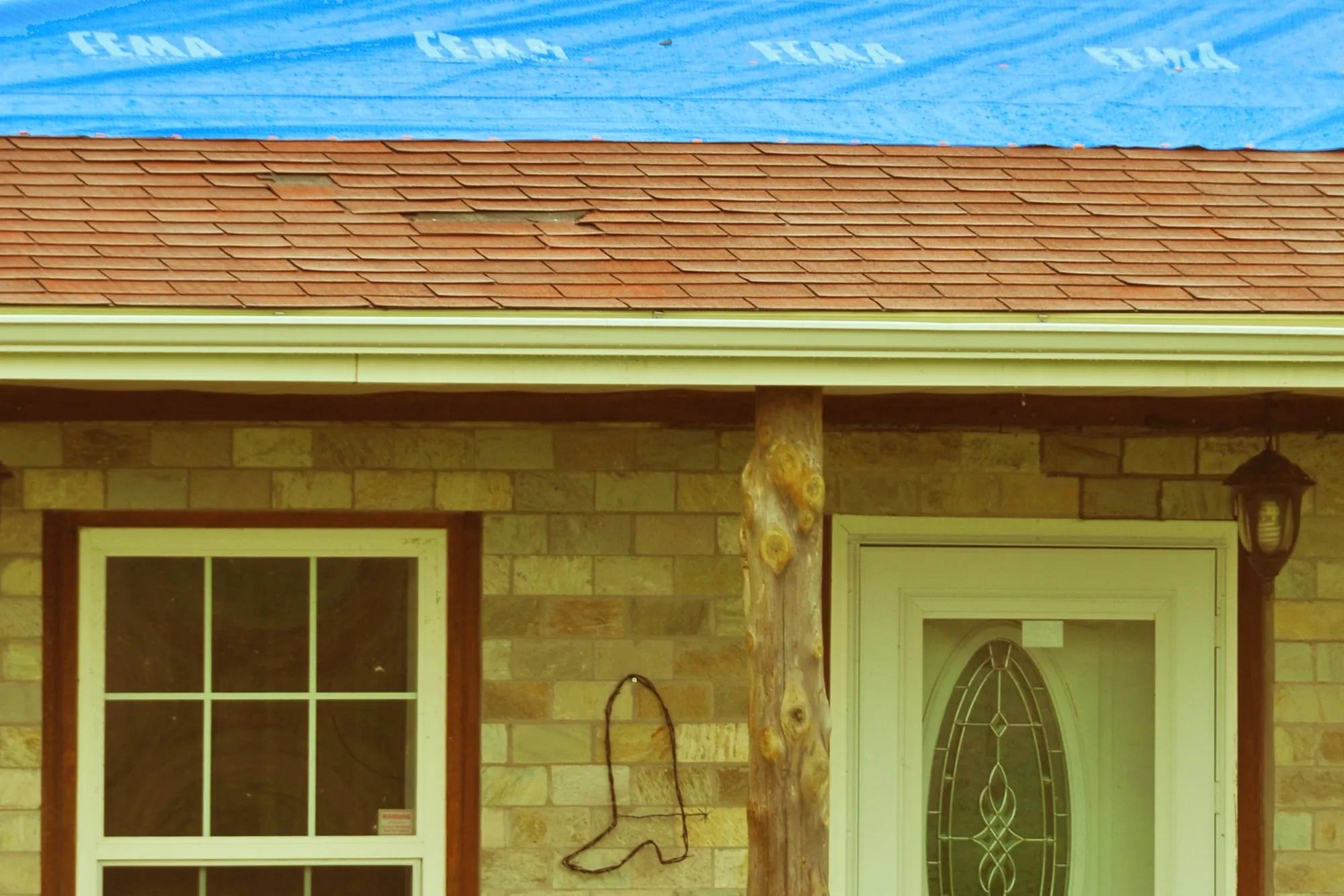 A blue tarp over a wind-damaged shingle roof