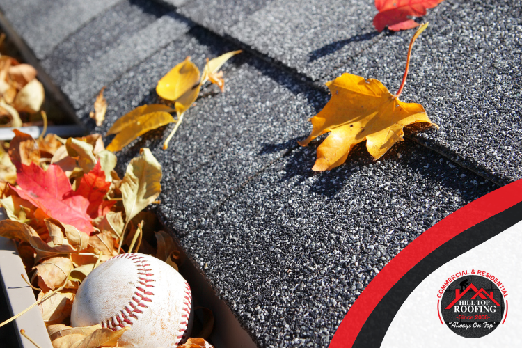 Close-up of a gutter filled with freshly fallen leaves and a baseball, showing the importance of fall inspections and maintenance.